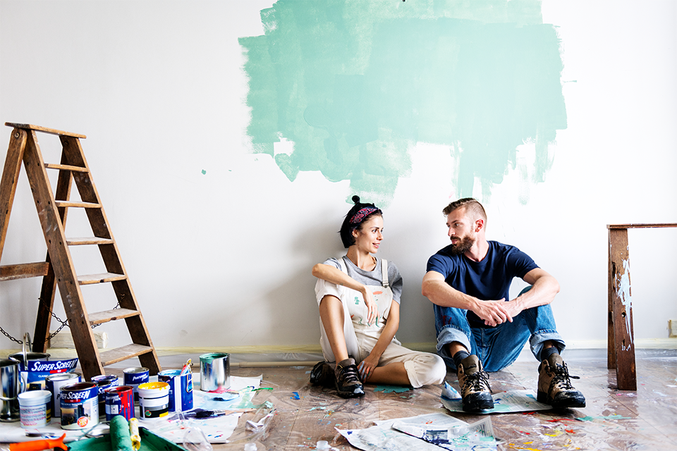 Couple sitting on the floor in front a partially painted wall