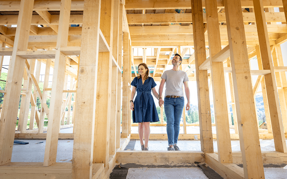 Wooden house frame with couple walking through to inspect