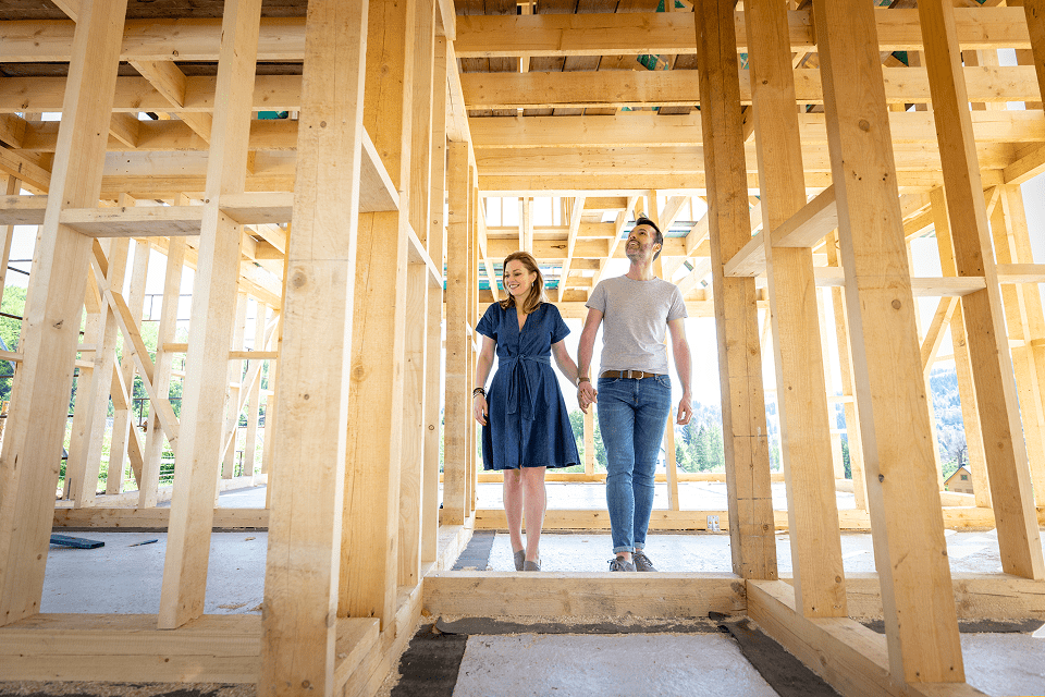 Wooden house frame with couple walking through to inspect